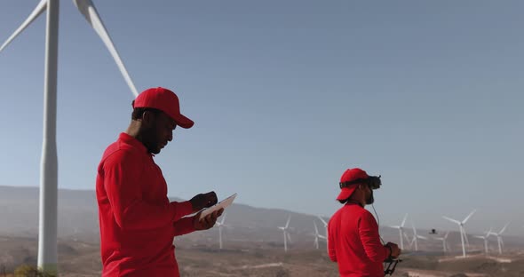 Multiracial engineer men working together on a windmill farm with digital tablet and drone