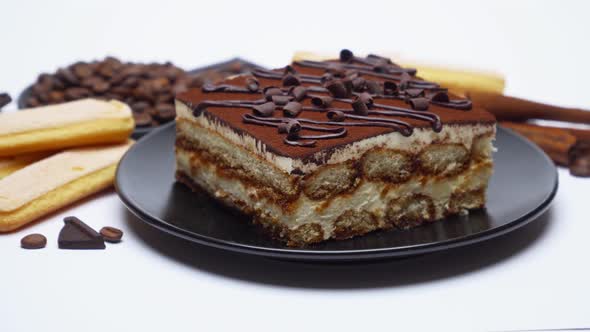 Portion of Traditional Italian Tiramisu dessert, coffee beans and savoiardi cookies on white