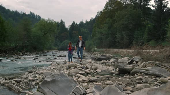 Woman and Man Walking on Rocks at River Bank