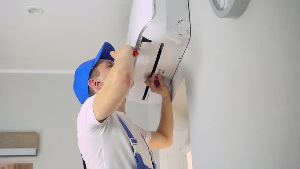 A young master in uniform repairs the air conditioner in the apartment.