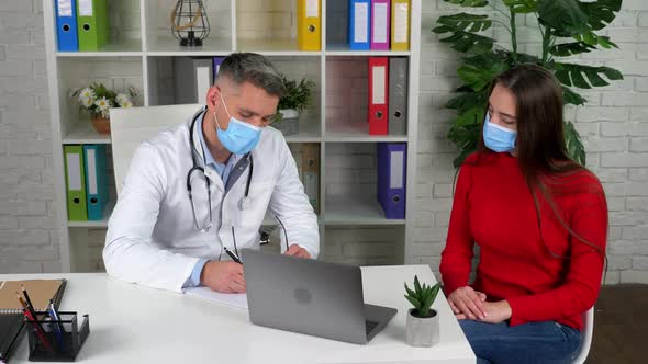 Doctor man and patient wears protective masks on faces in hospital communicates