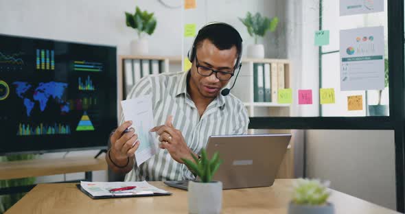 African American Office Worker Sitting in front of Computer and Explaining Report with Charts