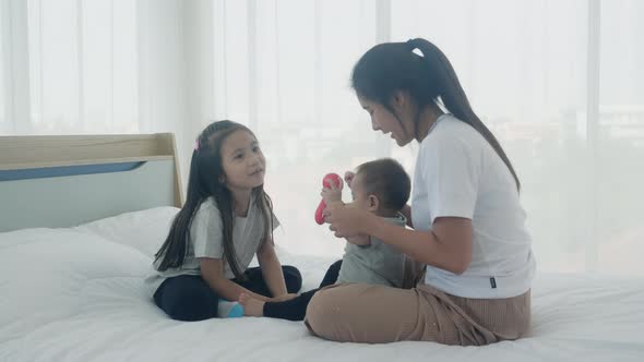 Young asian mother and daughter sitting playing with little baby girl on the bed together.