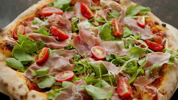 Delicious Pizza with Prosciutto Parma Ham Arugula Salad Rocket and Cherry Tomato on Rusty Dark