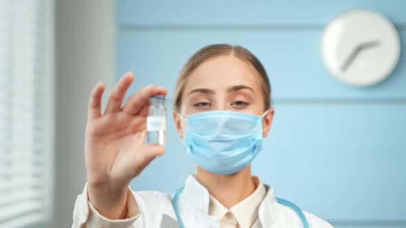 Young woman researcher in white coat and blue disposable face mask