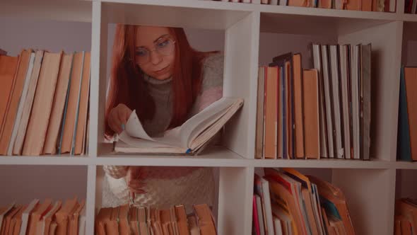 A Student is Reading a Book in the Library Behind the Bookshelves