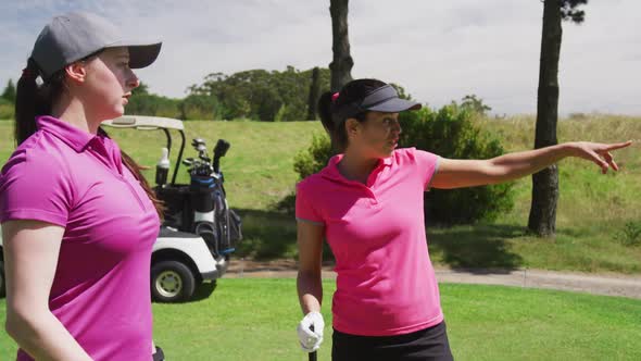 Two caucasian women playing golf one is pointing far away