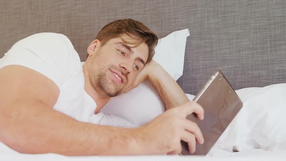 Smiling man lying on bed using his digital tablet 4K 4k