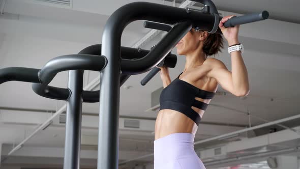 Mature Woman is Doing Pullups with Wide Grip in Gym Back View