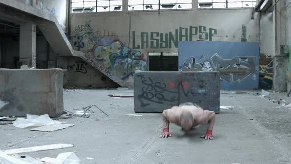 A shirtless personal trainer man does clapping pushups inside an abandoned building