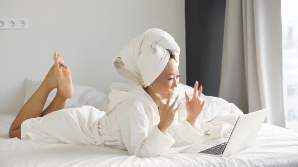 Happy Woman Welcomes Her Friend Family Online She Is Lying on the Bed with a Laptop