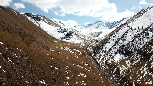 Mountain landscape with yellow grass. Peaks covered with snow. Flight on gorge