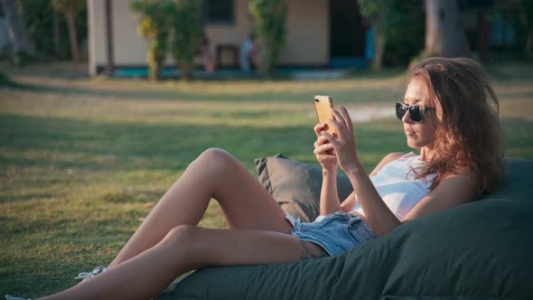 Young Caucasian Woman Using Her Smartphone While Lying on a Big Pillow