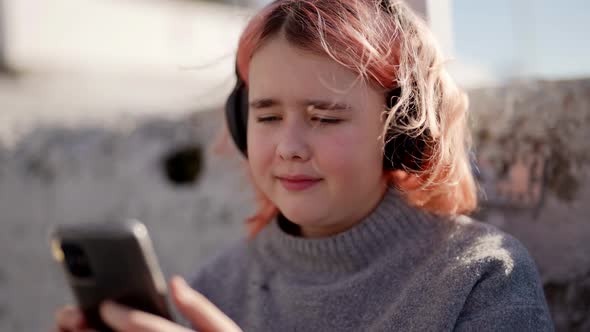 Chubby Schoolgirl with Wireless Headphones is Viewing Video in Smartphone