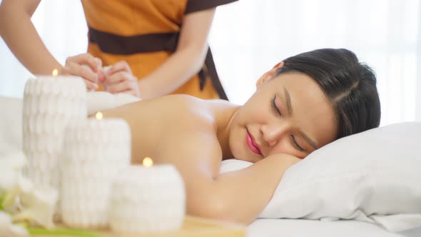 Asian beautiful woman enjoy thai hot compress massage with herbal bags for body care in spa salon.