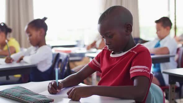 Portrait of african american schoolboy sitting in classroom, making notes