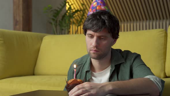 Sad Man Celebrates His Birthday Alone in the Living Room Blowing Out the Candles on the Cake