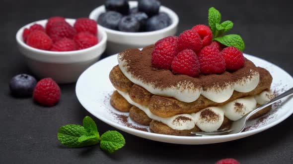 Portion of Classic Tiramisu Dessert with Raspberries and Blueberries on Dark Concrete Background