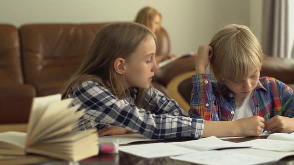 Cute Little Boy and Girl Studying at Home in The Foreground While Their Mother Is Sitting in The Background