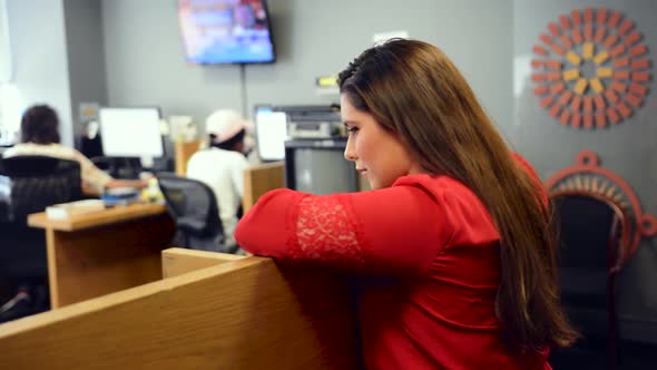 Woman in red shirt leans against cubical and observes coworkers