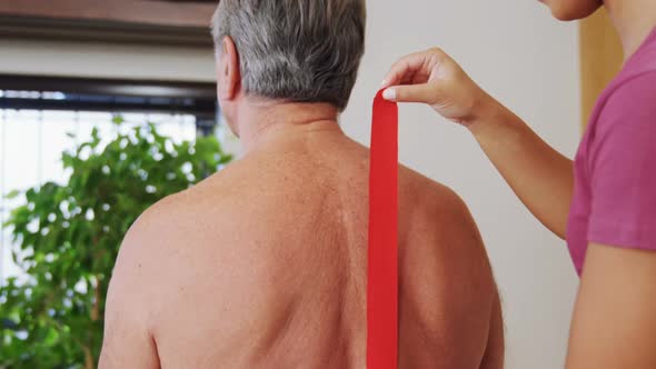 Physiotherapist sticking tape on senior patient back 4k