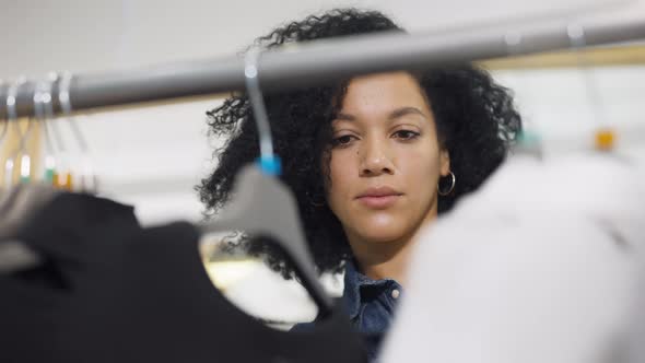 Beautiful African American Woman Choosing Clothes Hanging on Rack Hangers in Trendy Clothing Store