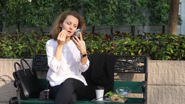 Young Business Woman Sitting Outdoors Having Lunch And Applying Makeup