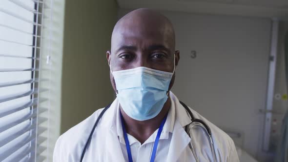 Portrait of african american male doctor wearing face mask standing in hospital room