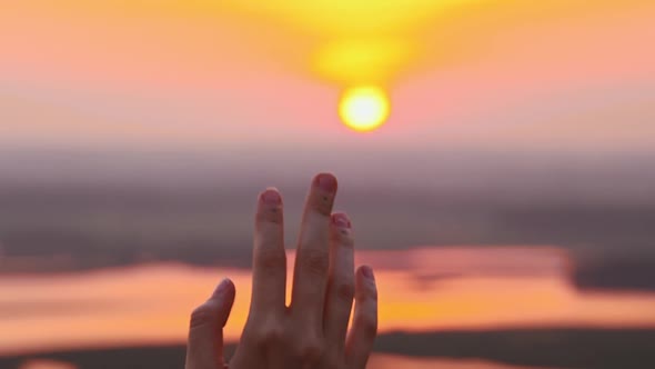 Hand of Young Woman Touching the Sunset Sun