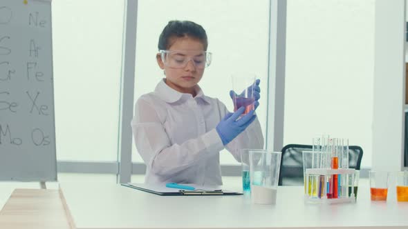 A Teenage Girl in a White Coat Aad Glasses Holds aFlask With a Chemical Solution