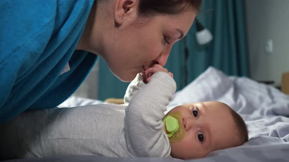 Young Mother Bends Kissing Hands of Baby Son Smiling Widely