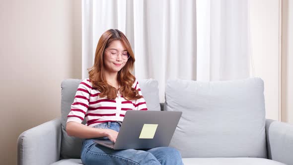 Young Asian woman sitting on sofa using notebook to shop online.