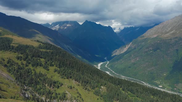 Aerial View of a Mountain River Flowing Through a Valley Under Snowcapped Mountain Peaks