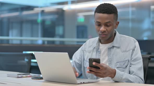 African Man with Laptop using Smartphone at Work