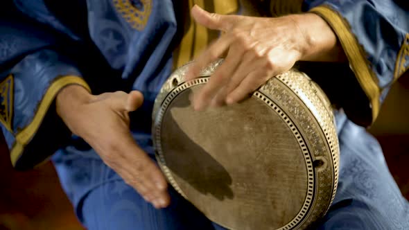 Tight shot of man in Moroccan dress playing arabic doumbek, darbuka, or derbeki