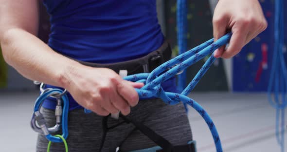 Midsection of caucasian woman securing rope in a harness belt at indoor climbing wall