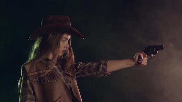 Girl Holds a Revolver in Her Hands and Aiming at the Villain. Black Smoke Background. Slow Motion