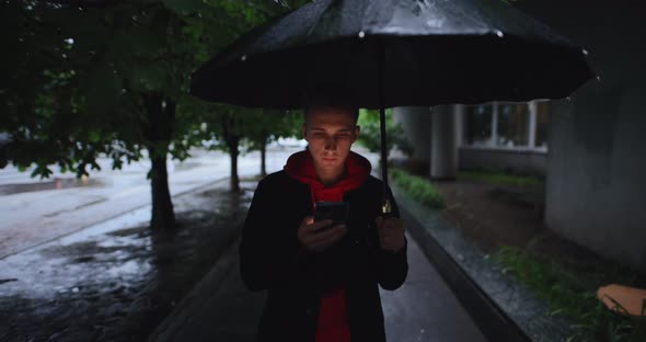 Man Walking at Alley Under Umbrella Using Smartphone