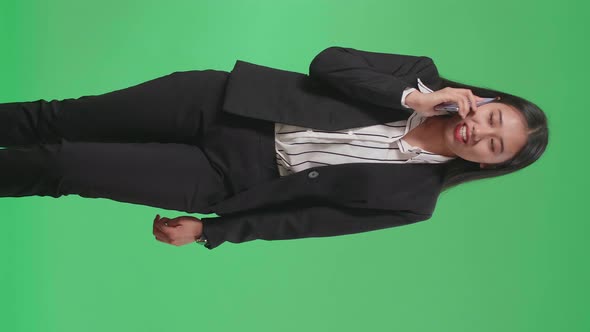 A Smiling Asian Business Woman Talking On Mobile Phone While Walking Through Green Screen