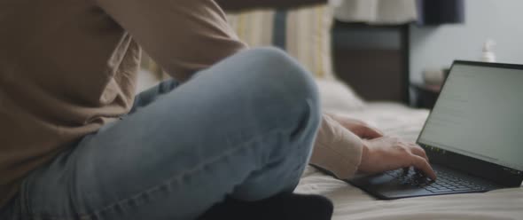 Man hands typing something on a laptop keyboard in the bedroom