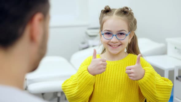 Cute Brunette Girl with Brown Eyes Looking at Camera Showing Thumbs Up Standing in Hospital