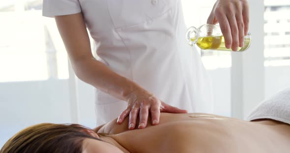 Masseur pouring massage oil on the back of her patient