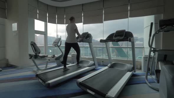 Clip of woman on the treadmill in fitness centre looking at window with cityscape Hong Kong, China