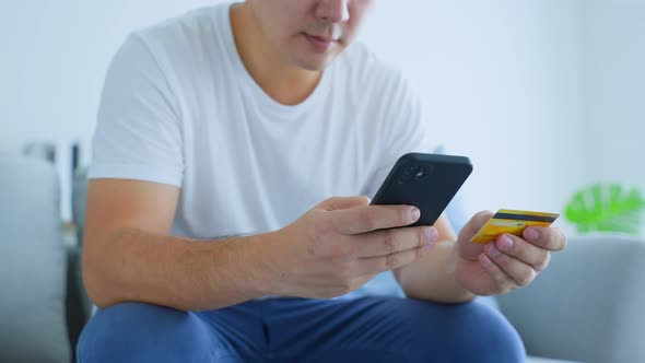 Close up of Asian male holding credit card to make e bank online after shopping online in house.