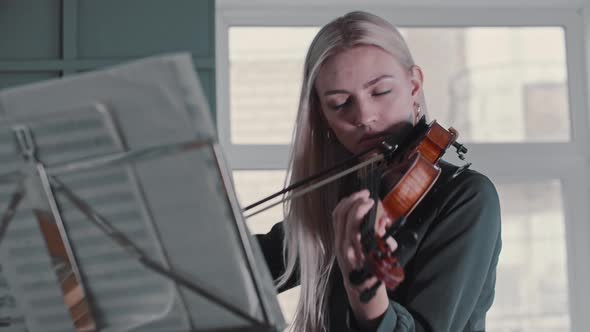 Young Blonde Woman Teacher Playing Violin By the Notes in the Class