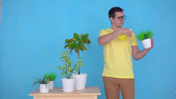 Man with Glasses Sprays Plants on the Table at Homelooking at the Camera Smiling