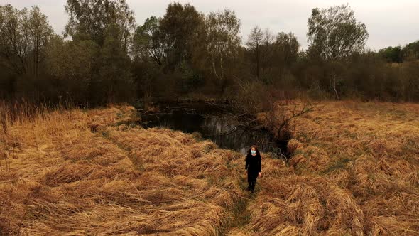 Woman in Protective Mask Goes By Path of Orange Grass