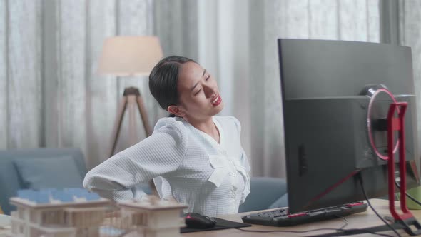 Asian Woman Engineer With The House Model Having A Backache While Working On A Desktop At Home