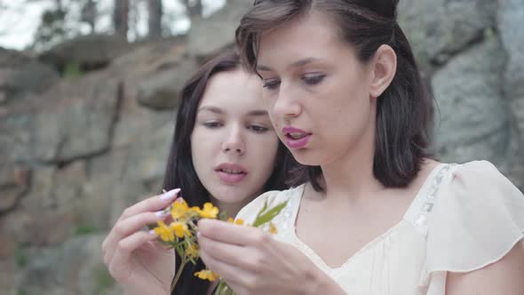 Portrait Two Beautiful Women with Black Hair Braid Flower Crown Near Huge Stone with Green Plants