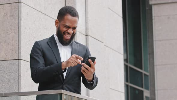 Excited Young African Ethnicity Millennial Bearded Man Looking at Mobile Phone Screen Reading